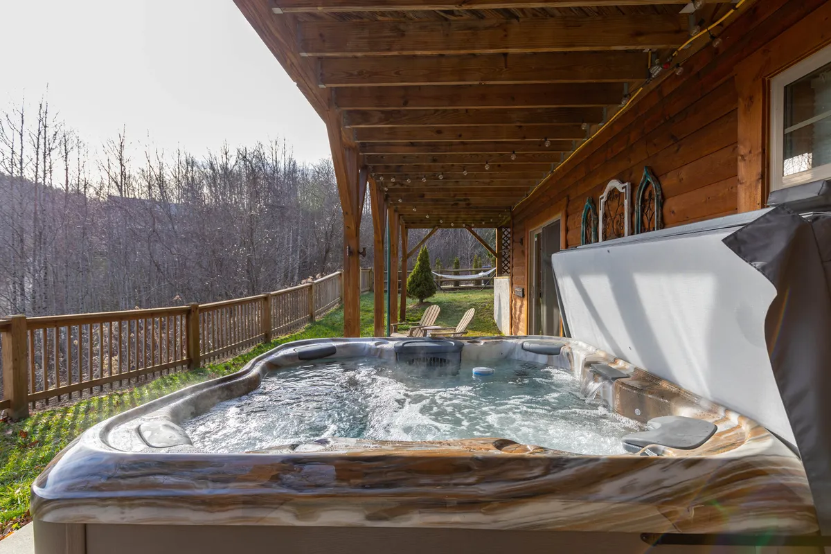 A serene hot tub on a wooden deck, overlooking lush nature and forested hills. The inviting water and tranquil surroundings offer the perfect spot to unwind after a day of adventure.