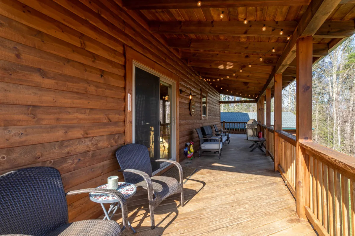 A cozy wooden porch illuminated by string lights, with rocking chairs and an open door, set against a peaceful natural backdrop. The scene evokes a sense of relaxed, social evenings and welcoming group get-togethers.